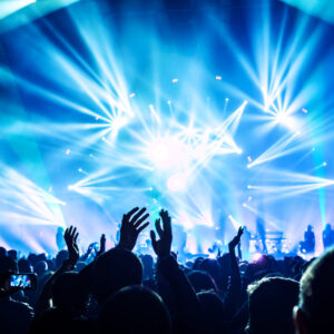 Large group of happy people enjoying rock concert, clapping with raised up hands, blue lights from the stage, new year celebration concept